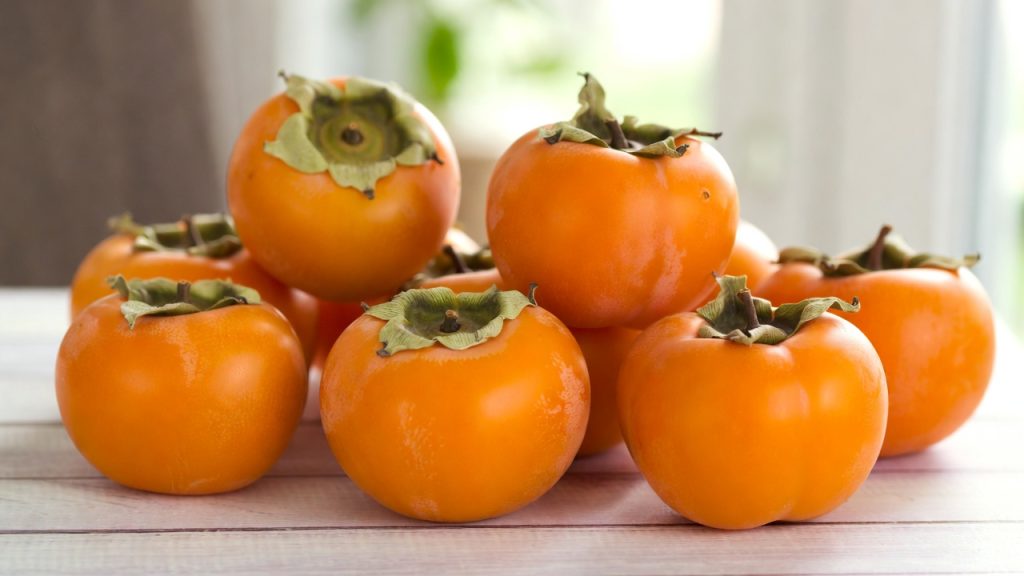 Kaki frais entier et coupé en deux montrant sa chair orange, fruit riche en bienfaits et facile à consommer.
